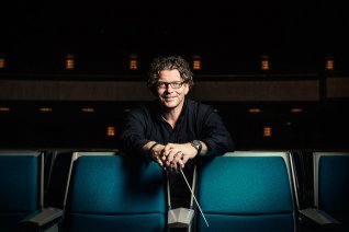 Dirigent Marcus Bosch in Zuschauerraum auf 2 Stühlen gelehnt